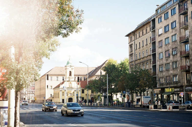 a street filled with lots of traffic next to tall buildings, unsplash, danube school, church in the background, sunny light, v ray, neo - classical style