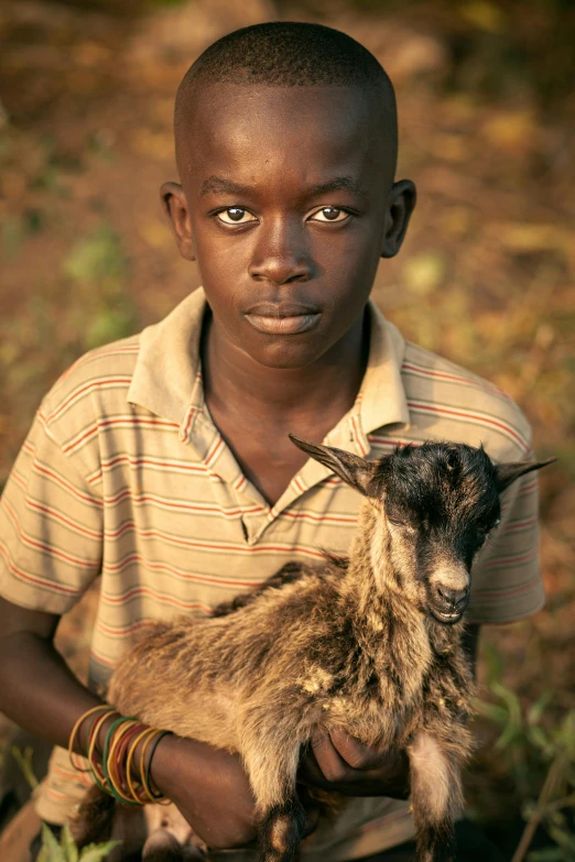 a young boy holding a goat in a field, dark skinned, award - winning photo ”