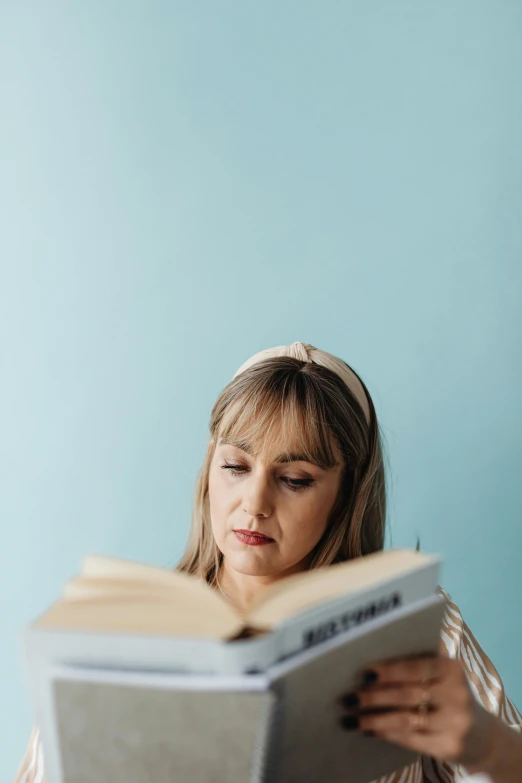 a woman sitting at a table reading a book, a portrait, pexels contest winner, with a blue background, curtain bangs, textbooks and books, over-shoulder shot