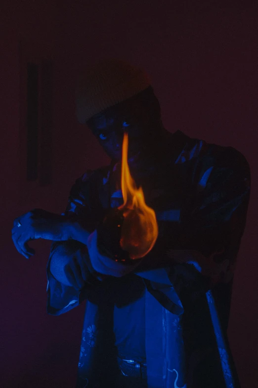 a man sitting on top of a chair next to a fire, an album cover, unsplash, conceptual art, all face covered with a fire, holding a glowing orb, bladee from drain gang, blue flame