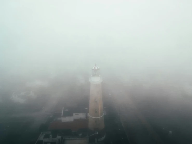 an aerial view of a lighthouse on a foggy day, a picture, by Eglon van der Neer, unsplash contest winner, surrealism, soft light.4k, low quality footage, city fog, brown