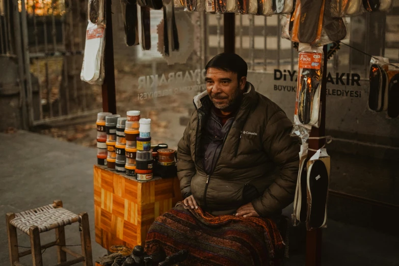 a man sitting on a bench in front of a store, crafts and souvenirs, portrait featured on unsplash, khyzyl saleem, winter season