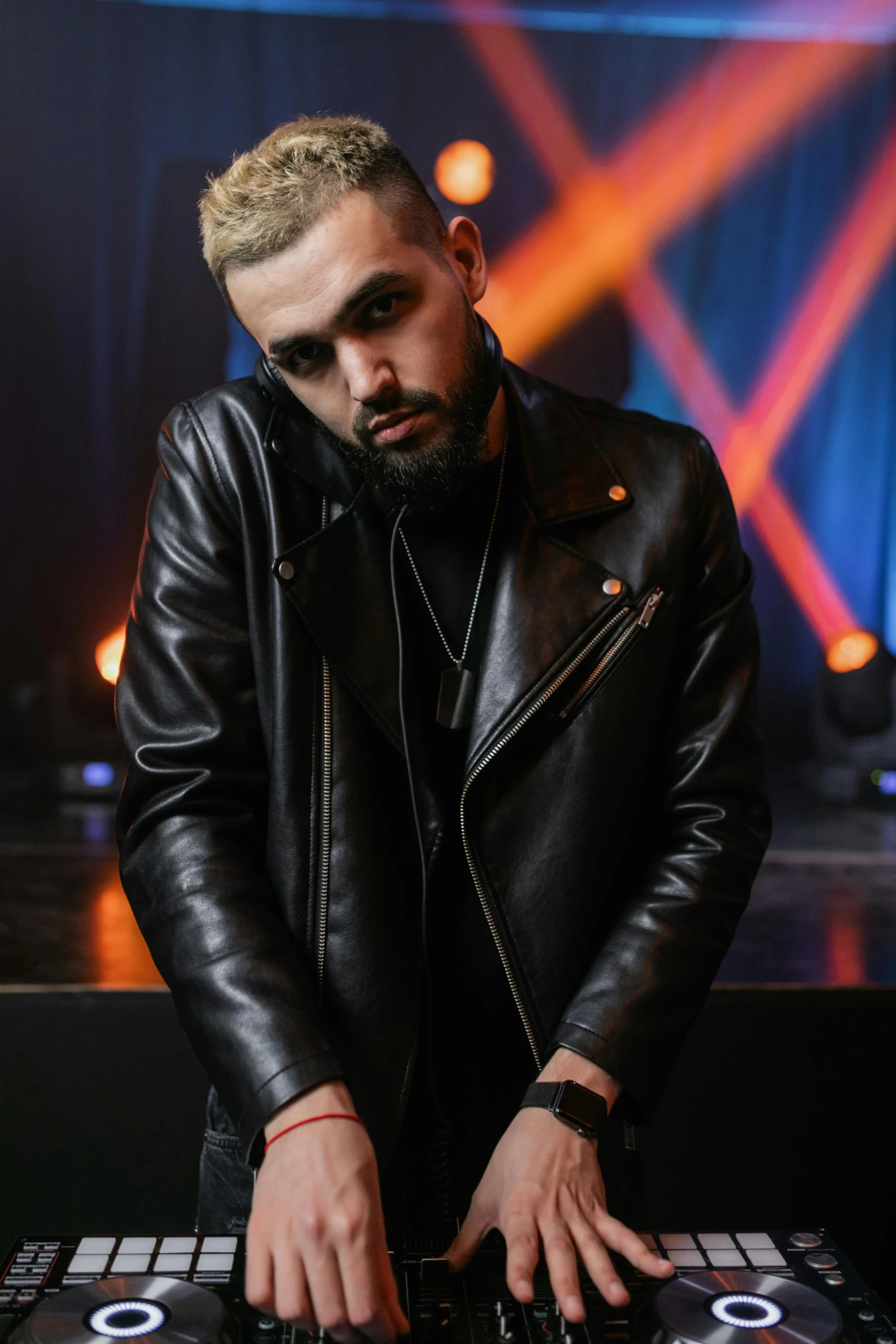 a man in a leather jacket mixing music on a mixer, an album cover, by Robbie Trevino, trending on pexels, photorealism, confident pose, wearing a full leather outfit, with a beard and a black shirt, a blond