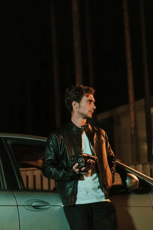 a man standing next to a car holding a camera, during the night, leather jackets, liam, asher duran