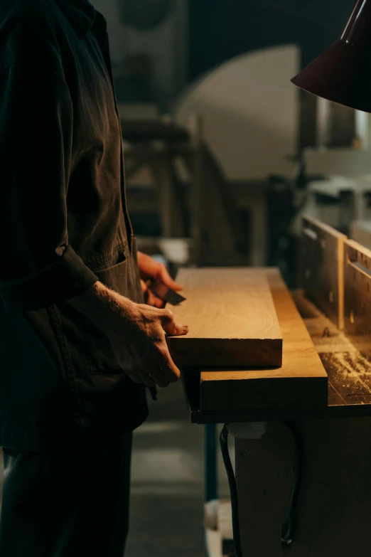 a man is working on a piece of wood, by Jessie Algie, trending on unsplash, private press, in a factory, hands on counter, close to night, french provincial furniture
