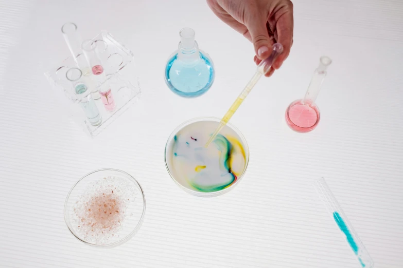 a white table topped with a cup filled with liquid, a microscopic photo, inspired by Helen Frankenthaler, trending on pexels, pathology sample test tubes, scales with magic powder, pregnancy, multicolored