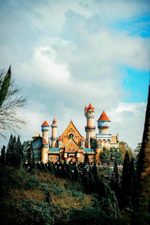 a castle sitting on top of a lush green hillside, inspired by disney, pexels contest winner, art nouveau, winter, colorful architecture, asymmetrical spires, movie photo