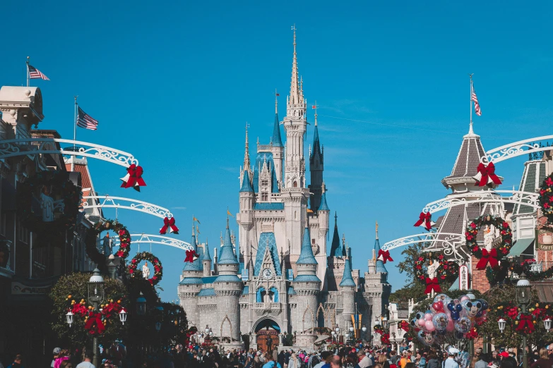 a crowd of people walking down a street in front of a castle, inspired by disney, pexels contest winner, clear blue skies, holiday season, amusement park interior design, 2 0 0 0's photo