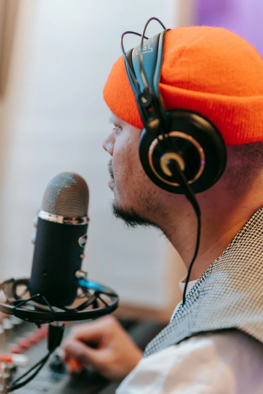 a man wearing headphones sitting in front of a microphone, with rap cap on head, studio orange, thumbnail, multiple stories