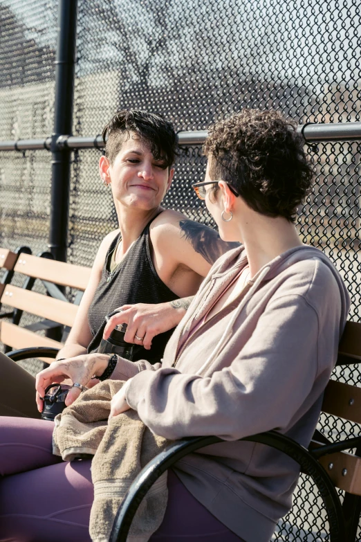 a couple of women sitting on top of a wooden bench, by Harriet Zeitlin, pexels, curly pixie cut hair, brooklyn, lesbian, talking