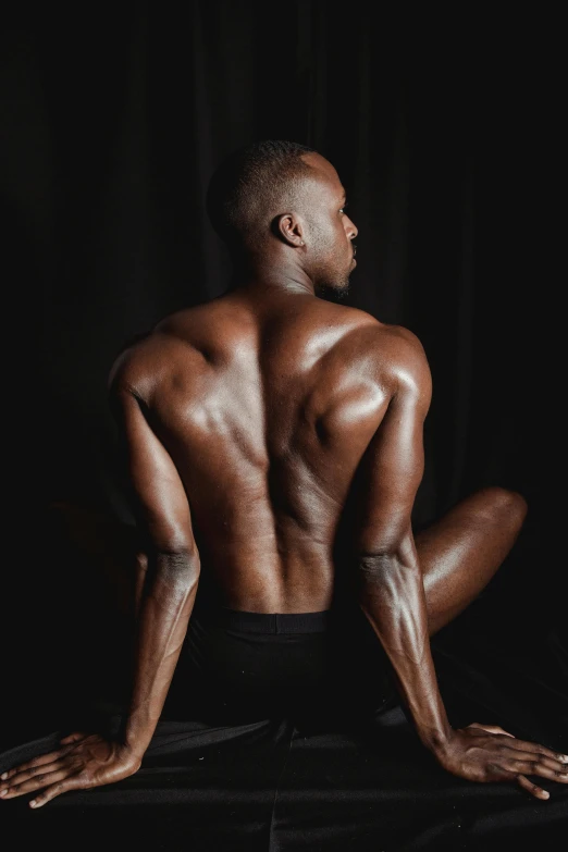a man sitting on a table with his back to the camera, by Jessie Alexandra Dick, pexels contest winner, hyperrealism, ifbb fitness body, pitch black skin, back arched, high arches