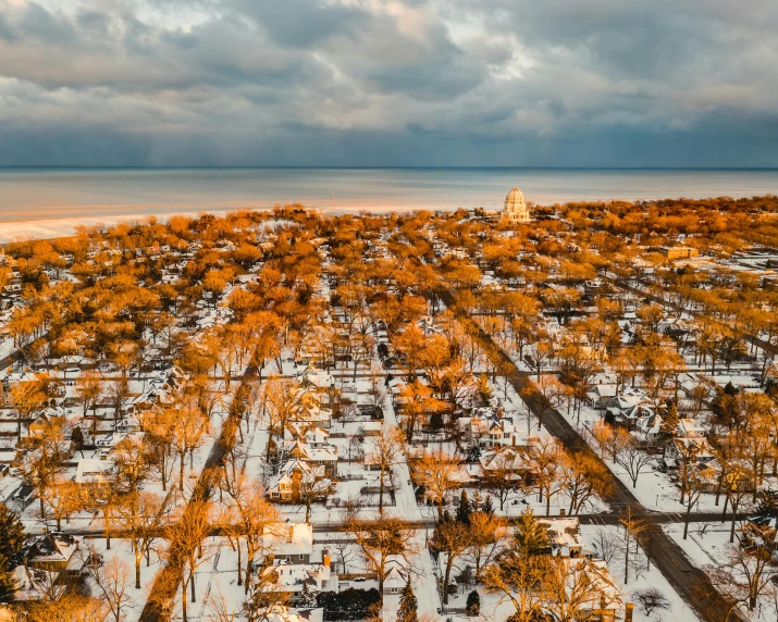 an aerial view of a city covered in snow, a colorized photo, by Carey Morris, unsplash contest winner, surrealism, cemetery, shoreline, midwest town, orange skies