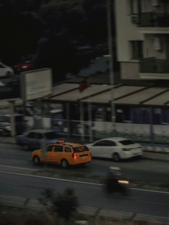 a yellow car driving down a street next to tall buildings, by Attila Meszlenyi, vhs footage of a movie set, istanbul, orange, **cinematic