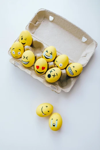 a carton of eggs with smiley faces painted on them, a picture, trending on pexels, on a white table, new emoji of biting your lip, photo session, ██full of expressions██