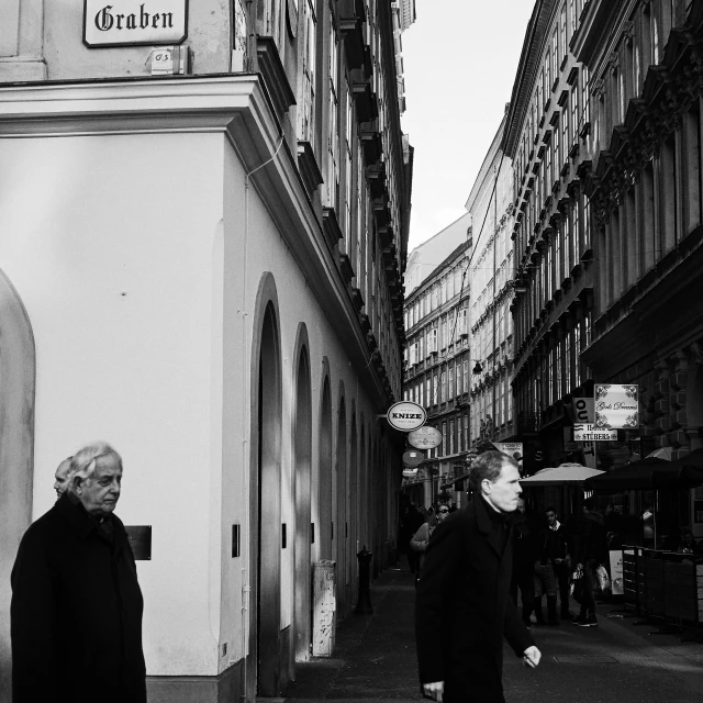 a couple of people that are walking down a street, a black and white photo, viennese actionism, old shops, white-haired, sad men, surrounding the city