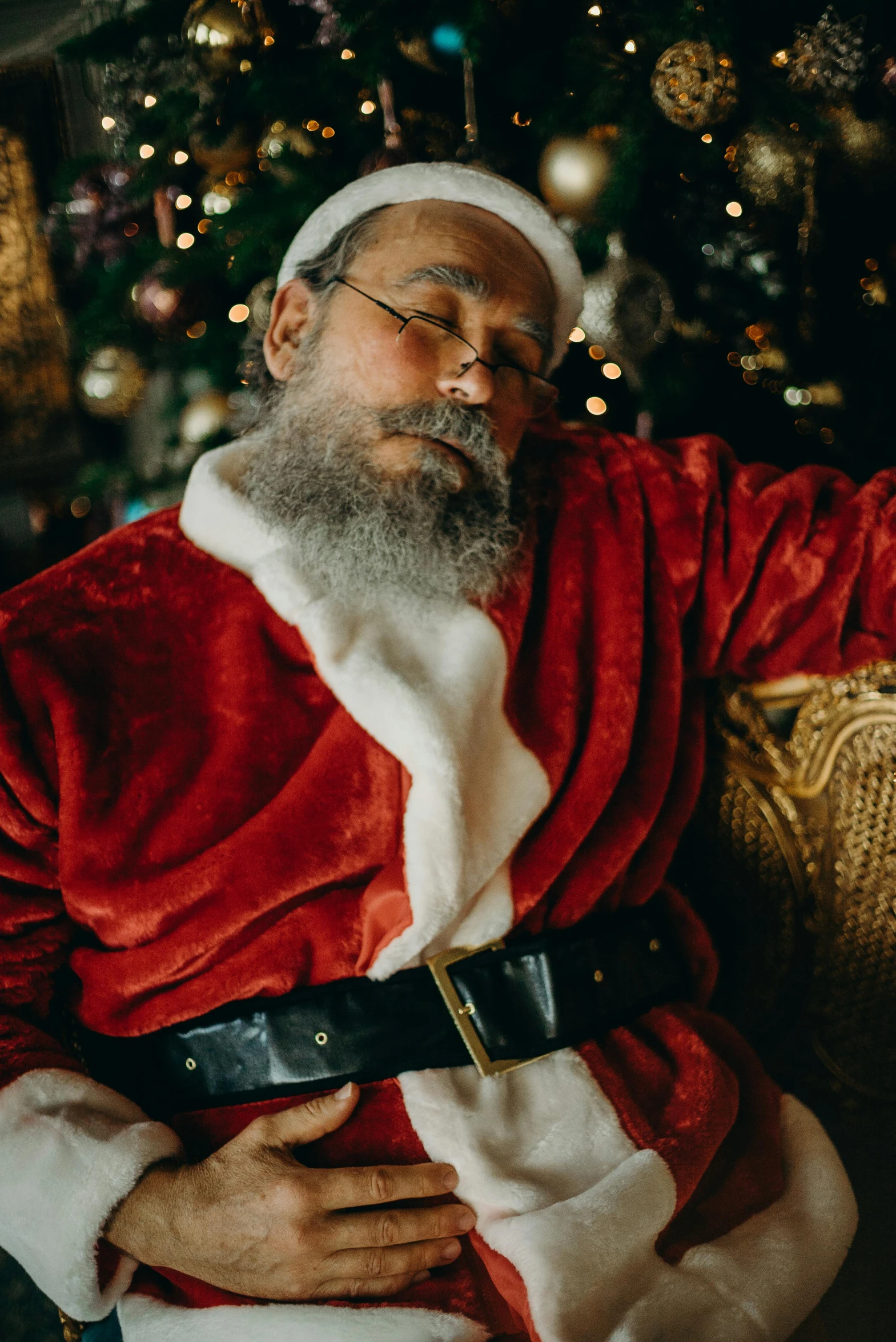 a man in a santa suit sitting in front of a christmas tree, pexels, renaissance, sleeping, grey trimmed beard, resting on chest, eyes closed