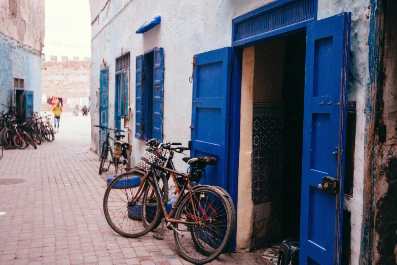 a couple of bikes parked in front of a blue door, by Julia Pishtar, pexels contest winner, les nabis, moroccan city, 🦩🪐🐞👩🏻🦳, gold and indigo, thumbnail