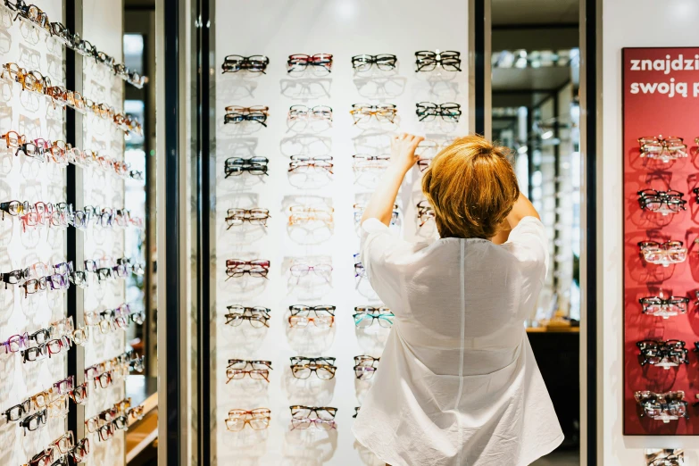 a woman standing in front of a wall of glasses, at checkout, glasses |, lachlan bailey, filling the frame