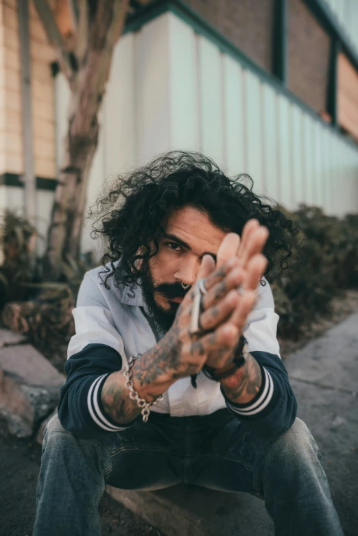 a man sitting on a curb with his hands in the air, an album cover, inspired by Jeremy Henderson, pexels contest winner, gunplay, mexican mustache, looking away from camera, profile image