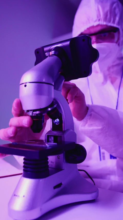 a person in a lab coat looking through a microscope, by Dan Luvisi, shutterstock, holography, purple filter, photograph credit: ap, gif, high angle shot