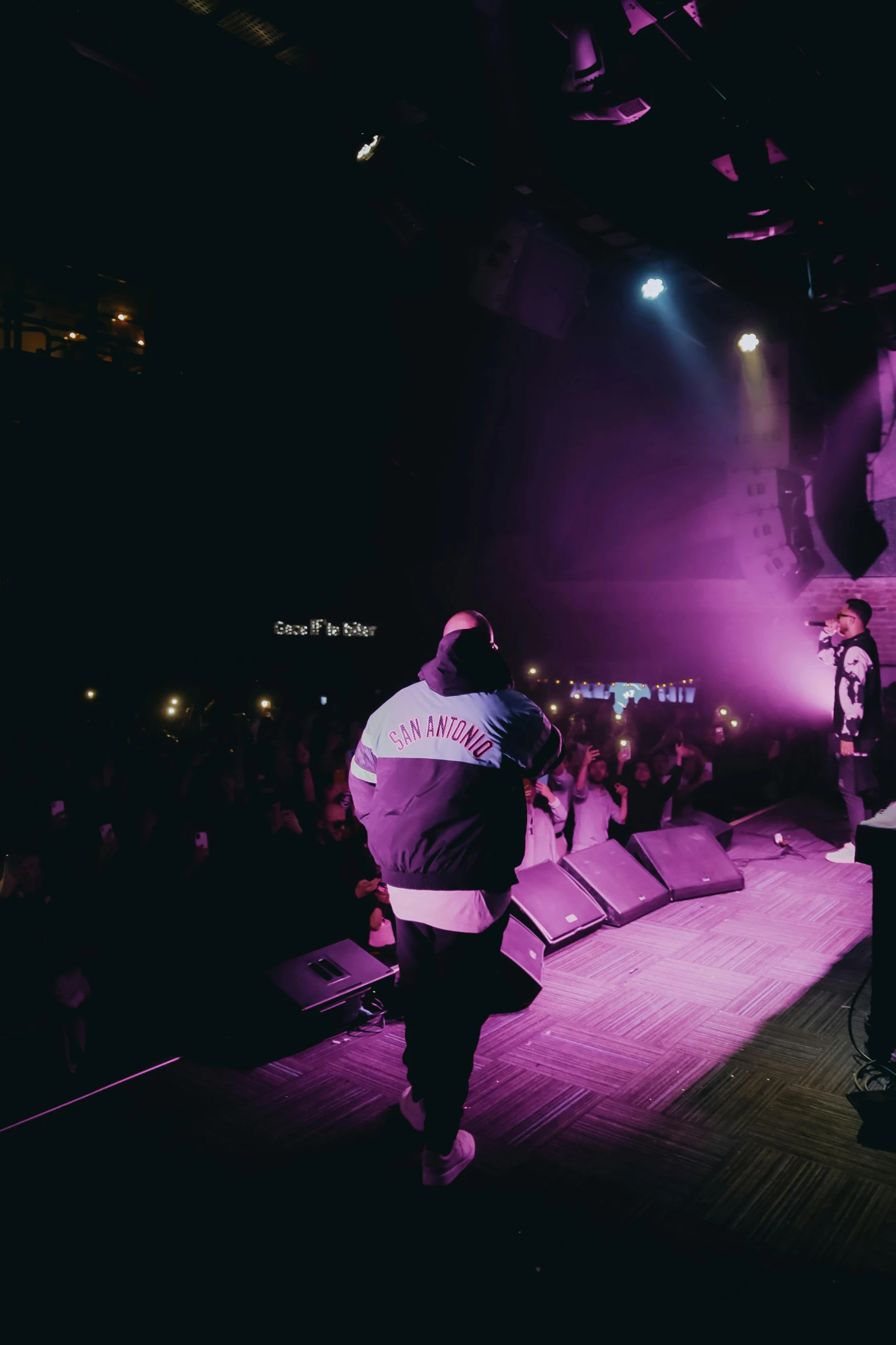 a group of men standing on top of a stage, a picture, by Robbie Trevino, teddy fresh, panoramic, night life, medium shot taken from behind