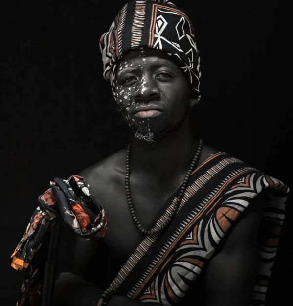 a man with black paint on his face, an album cover, by Ingrida Kadaka, pexels contest winner, afrofuturism, traditional clothes, professional body paint, 2019, panel of black