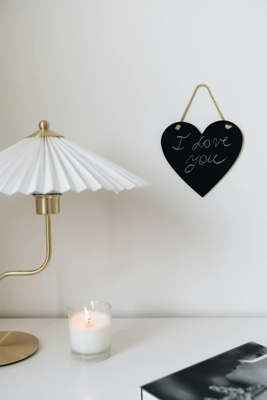 a white table topped with a lamp next to a book, a picture, rose gold heart, blackboard, parasol, dark. no text