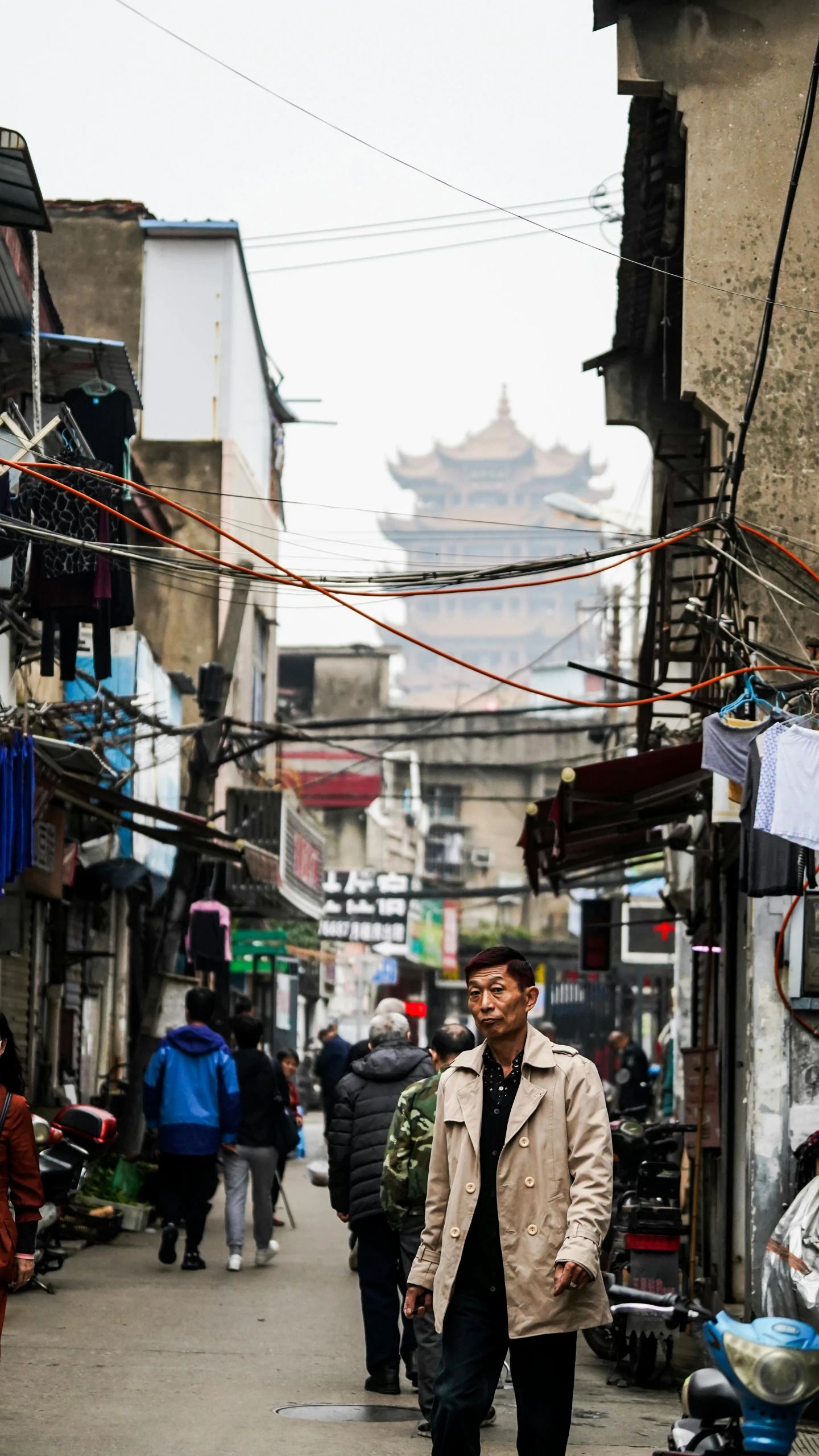 a man walking down a street next to a building, inspired by Zhang Sengyao, trending on unsplash, mingei, town in the background, vendors, wires hanging above street, ancien chinese tower