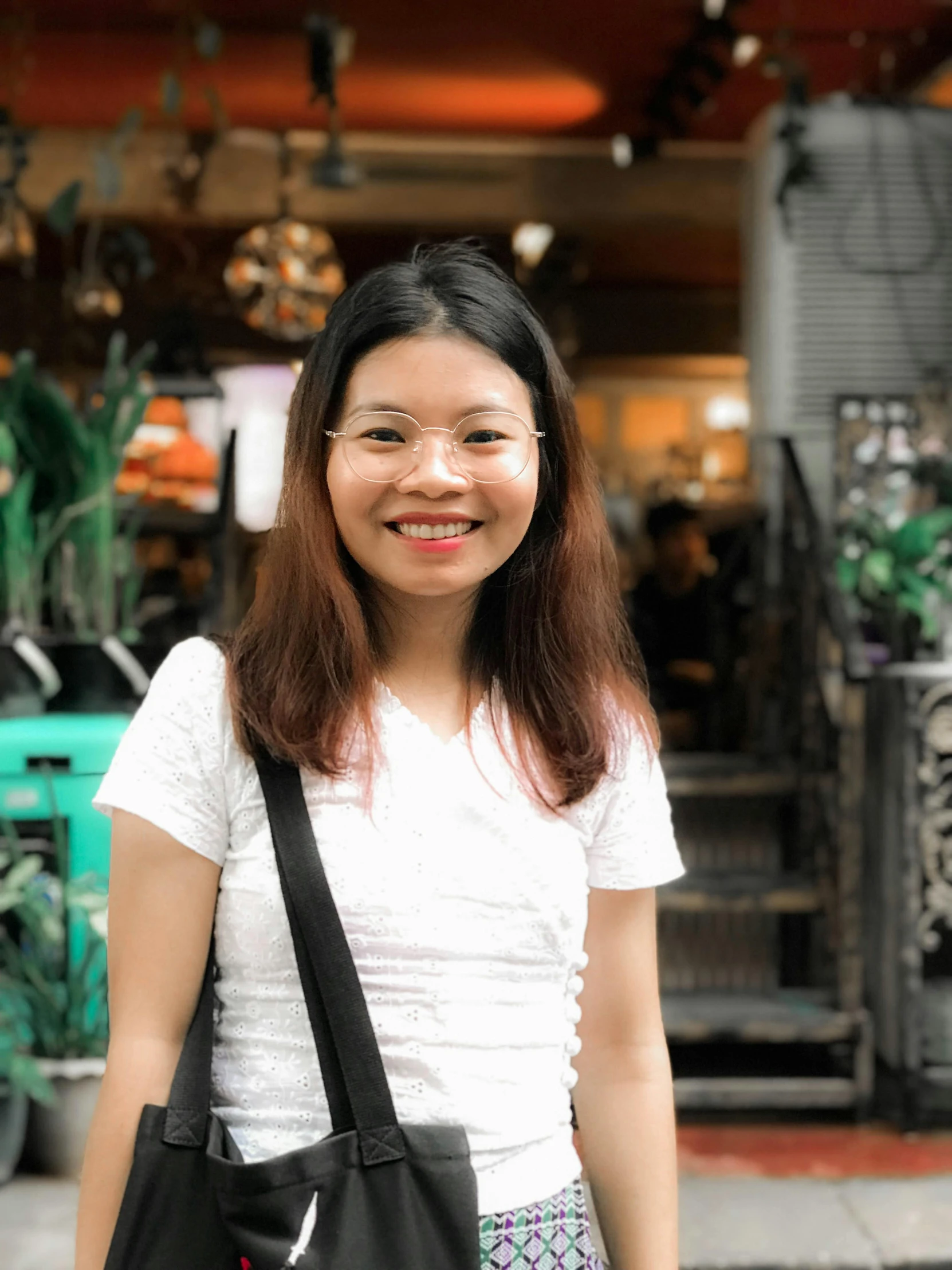 a woman standing on a sidewalk in front of a store, a picture, inspired by Ruth Jên, pexels contest winner, headshot profile picture, malaysian, with square glasses, low quality photo