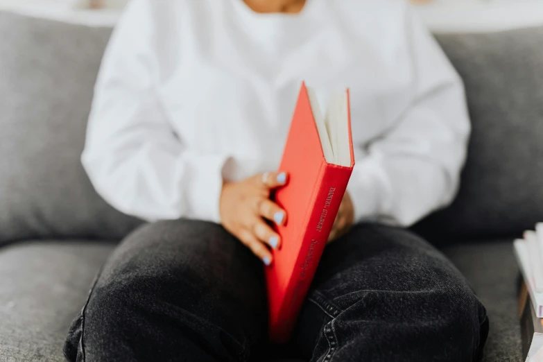 a woman sitting on a couch reading a book, pexels contest winner, figuration libre, white t-shirt with red sleeves, red sweater and gray pants, uncropped, lgbtq