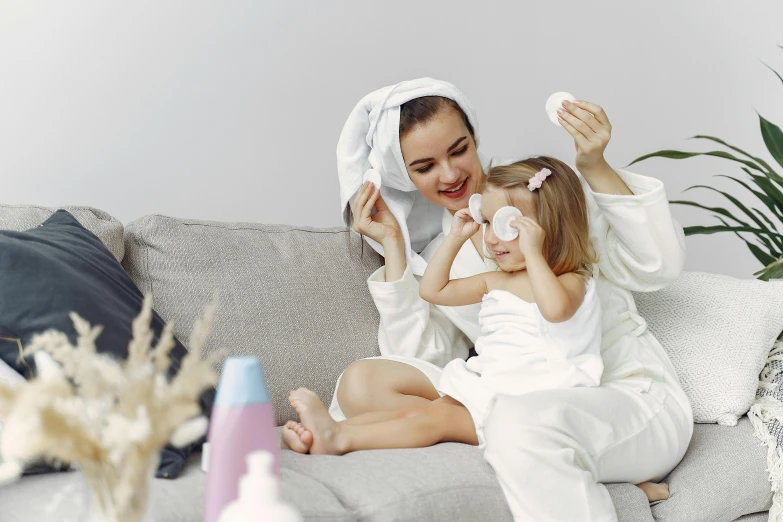 a woman and a little girl sitting on a couch, skincare, wearing a grey robe, clean image, wearing a towel