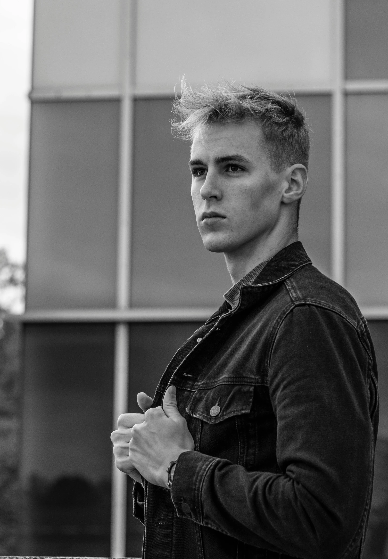 a man standing in front of a building, a black and white photo, inspired by Anthony Devas, pexels contest winner, blonde and attractive features, people with mohawks, caspar david, square masculine jaw