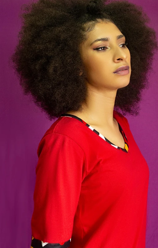 a woman standing in front of a purple background, by Chinwe Chukwuogo-Roy, pexels, long hair and red shirt, with afro, young woman, various posed
