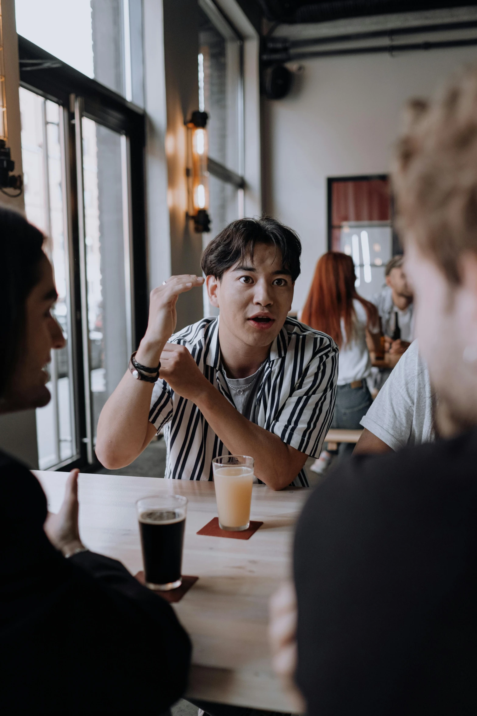 a group of people sitting around a wooden table, pexels contest winner, asian man, talking, non-binary, holding a beer