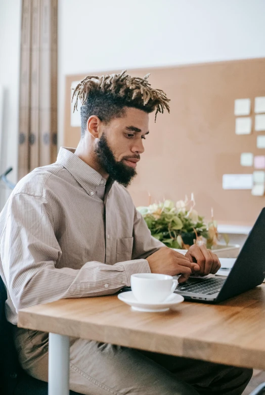 a man sitting at a table working on a laptop, trending on pexels, renaissance, hair styled in a bun, mixed race, scruffy man, post graduate