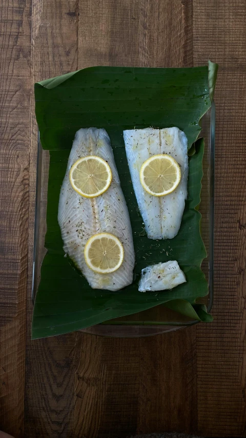 a couple of fish sitting on top of a banana leaf, on a wooden tray, thumbnail, with lemon skin texture, centred