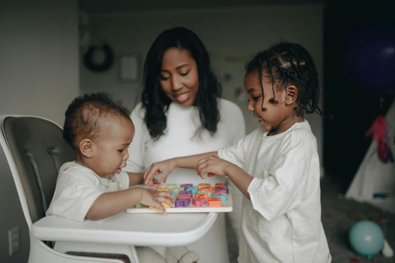 a woman and two children sitting in a high chair, pexels contest winner, board games on a table, avatar image, diverse, black