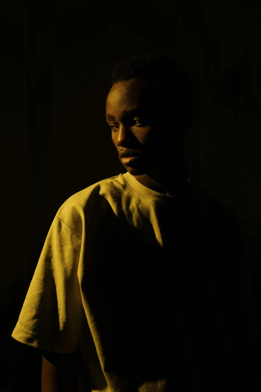 a man standing in a dimly lit room, inspired by Gordon Parks, adut akech, with yellow cloths, portrait top light, : kendrick lamar