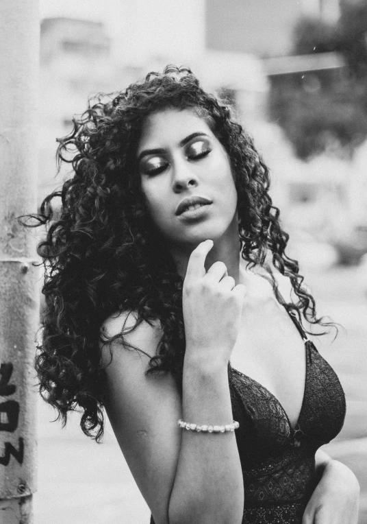 a black and white photo of a woman with curly hair, inspired by Briana Mora, in a black betch bra, r&b, persian queen, street photo