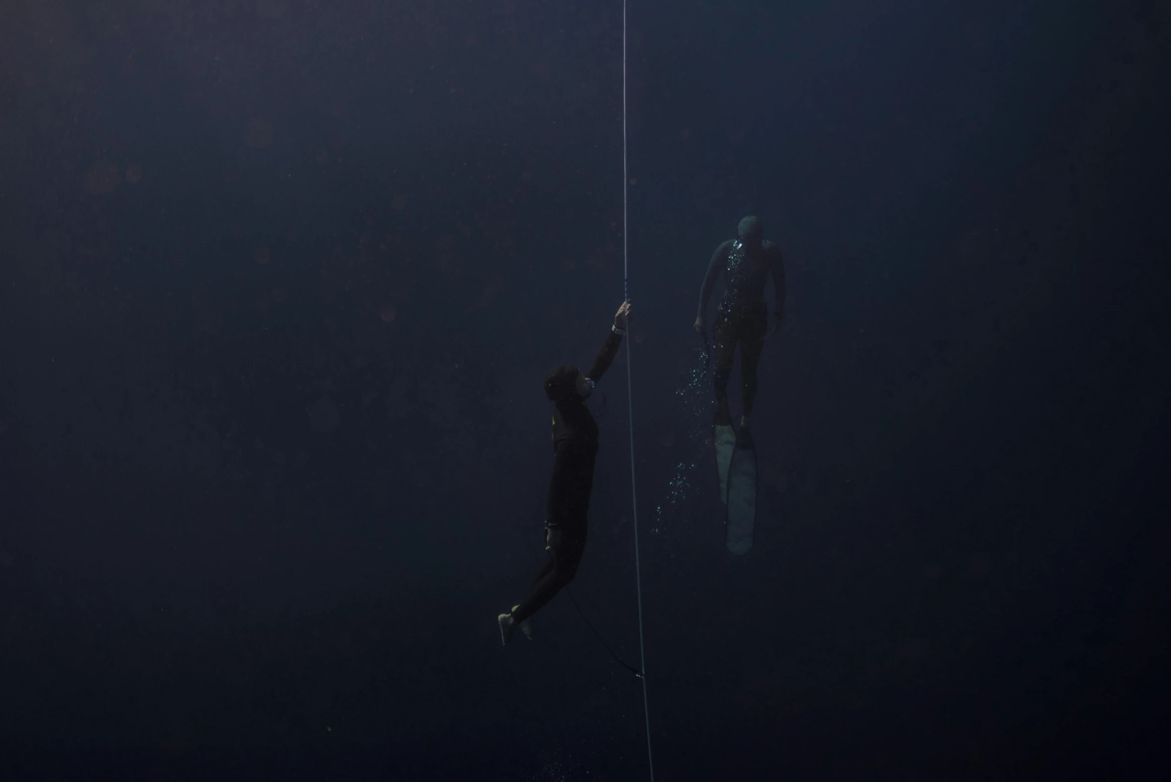 a couple of people that are in the water, by Elsa Bleda, conceptual art, hanging rope, man in dark blue full body suit, denis villeneuve movie still, subsurface scandering