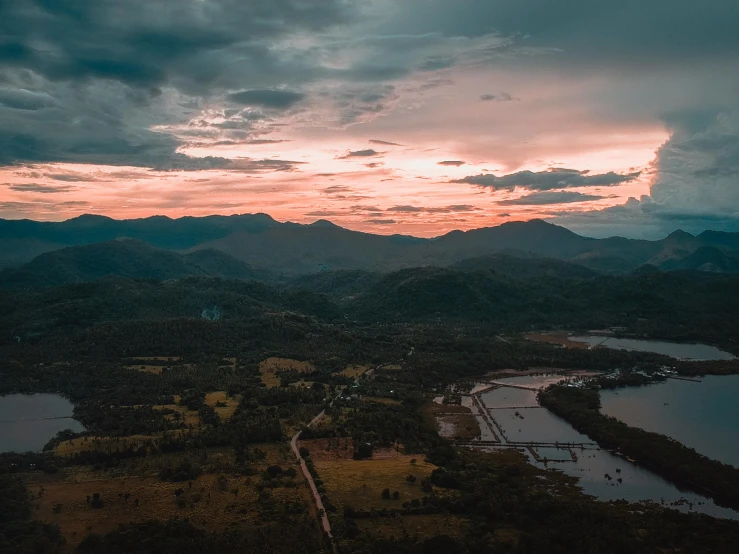 a sunset over a lake with mountains in the background, pexels contest winner, happening, aerial view of an ancient land, paddy fields and river flowing, thumbnail, distant mountains lights photo