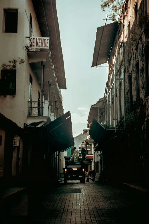 a truck driving down a narrow street next to tall buildings, a picture, inspired by Elsa Bleda, pexels contest winner, renaissance, city of armenia quindio, cave town, photo taken on fujifilm superia, late afternoon light