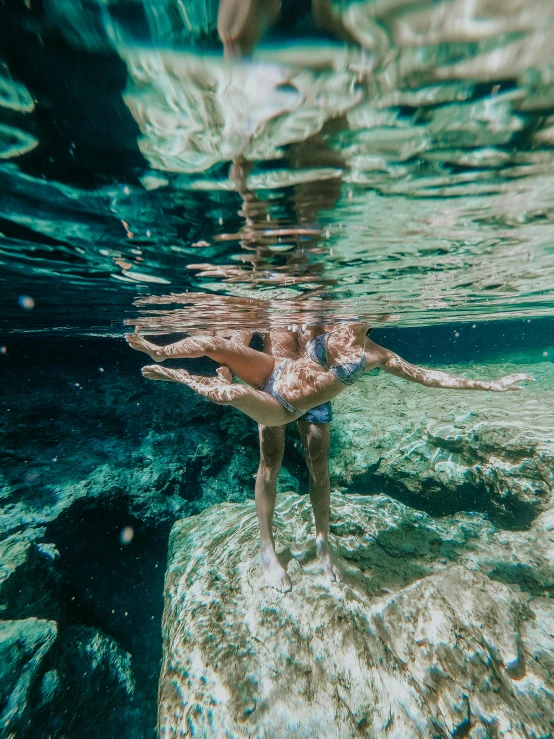 a person swimming in a body of water, crystal clear water, under water, lush surroundings, upsidedown