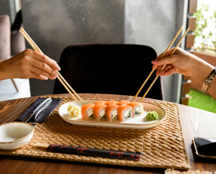 a person holding chopsticks over a plate of sushi, sitting at a table, ayahausca, unbeatable quality, fan favorite