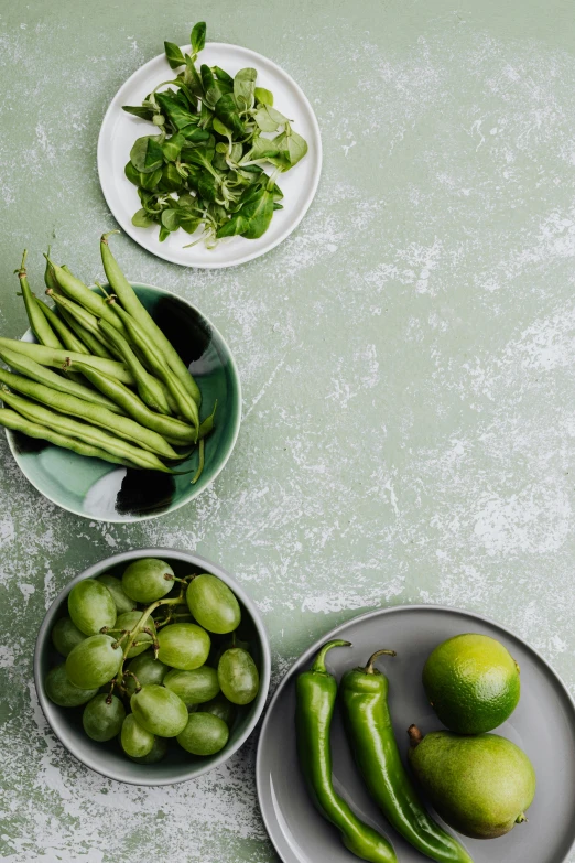 a table topped with bowls filled with green vegetables, a still life, inspired by Art Green, unsplash, on grey background, lime, beans, green wall