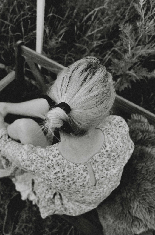 a black and white photo of a little girl sitting on a bench, a black and white photo, pexels, romanticism, blond hair. ponytail, back of head, in the countryside, photo of a woman