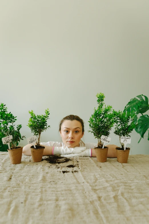 a woman sitting at a table with potted plants, inspired by Sarah Lucas, pexels contest winner, trees growing on its body, sydney sweeney, promotional image, seedlings