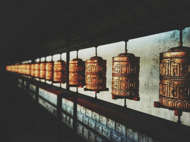 a row of bells hanging from the side of a wall, by Daniel Lieske, trending on unsplash, cloisonnism, warm lantern lighting, brown, thangka, medium format. soft light