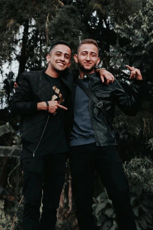 two men standing next to each other in front of trees, an album cover, by Robbie Trevino, pexels contest winner, smiling couple, wearing black clothes, thiago alcantara, profile image