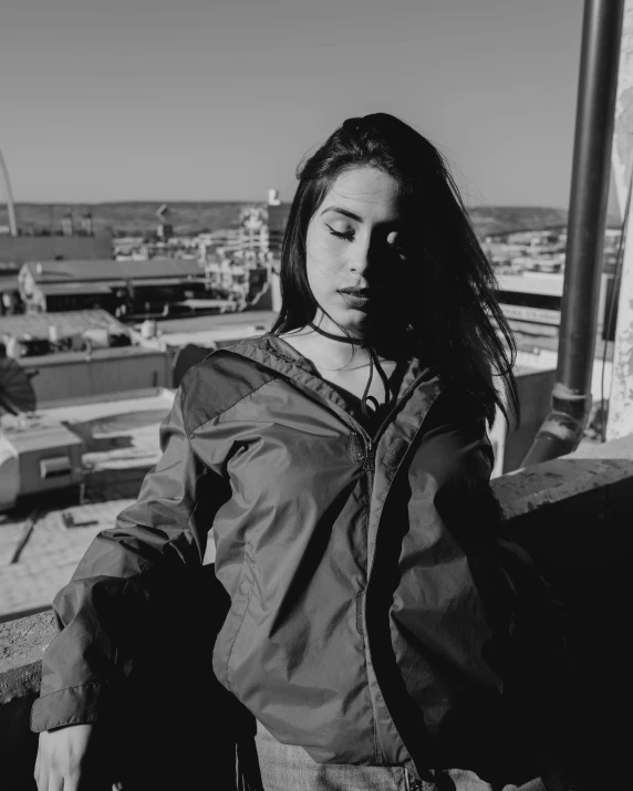 a black and white photo of a woman on a balcony, a black and white photo, inspired by Elsa Bleda, pexels contest winner, realism, black haired girl wearing hoodie, techwear look and clothes, pale-skinned persian girl, red jacket